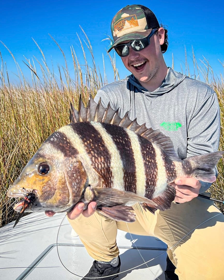 Man holding a large sheepshead on a boat with grass and blue sky in the background