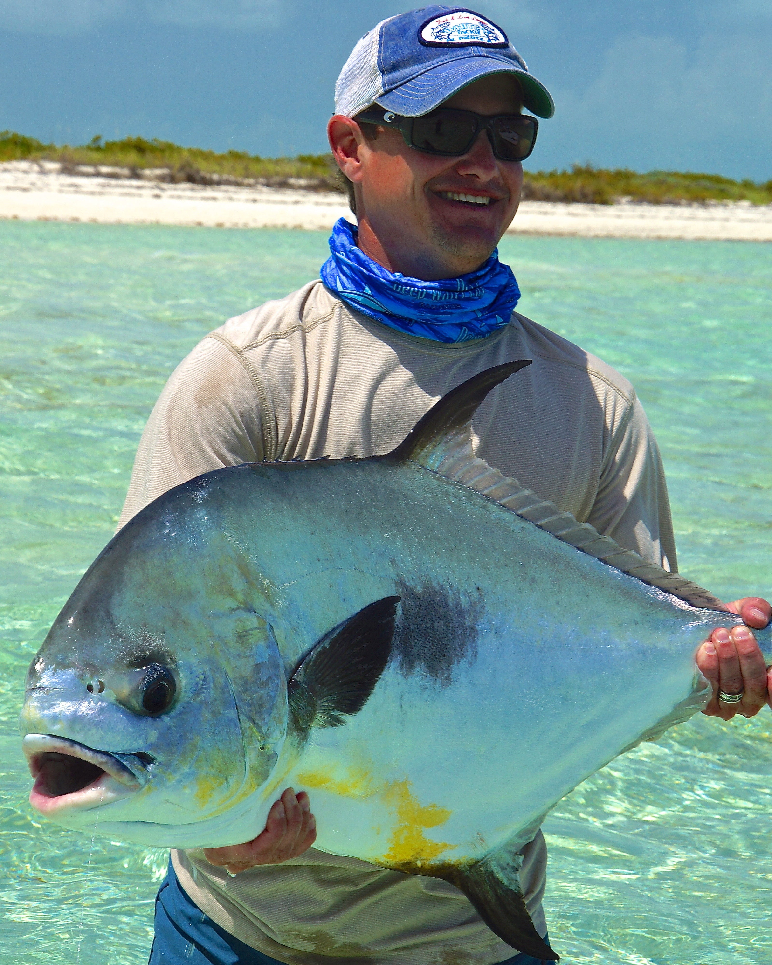 Man holding a large permit in clear water with a tropical island in the background