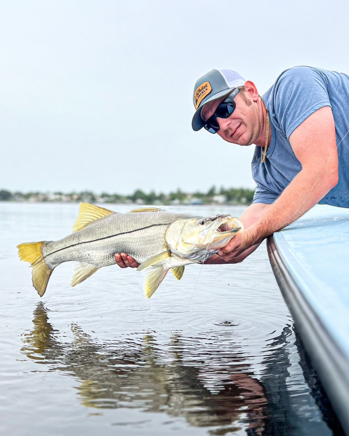 Man holding a large fsnook on a river with a boat in the background