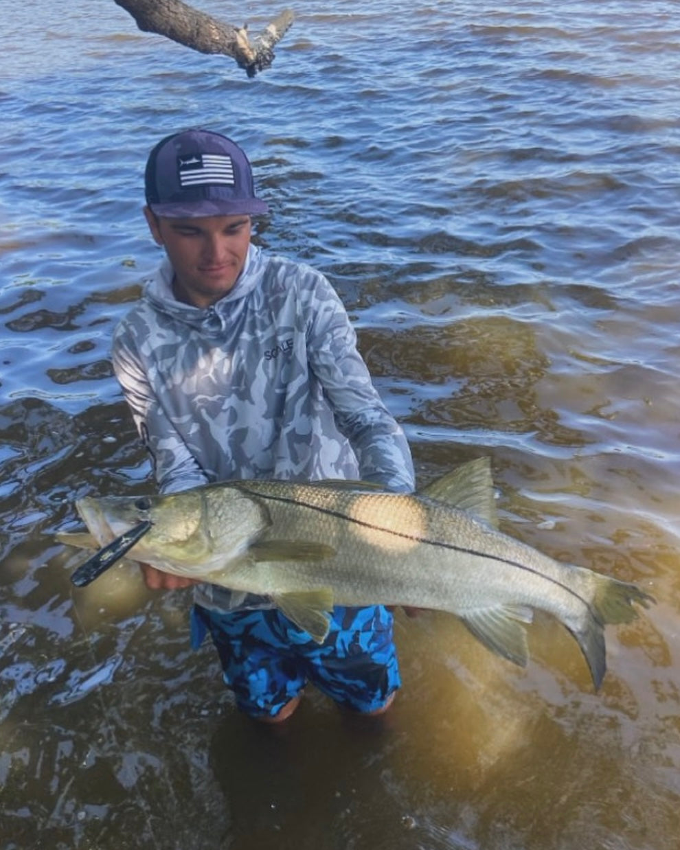 man holding a large snook in shallow water