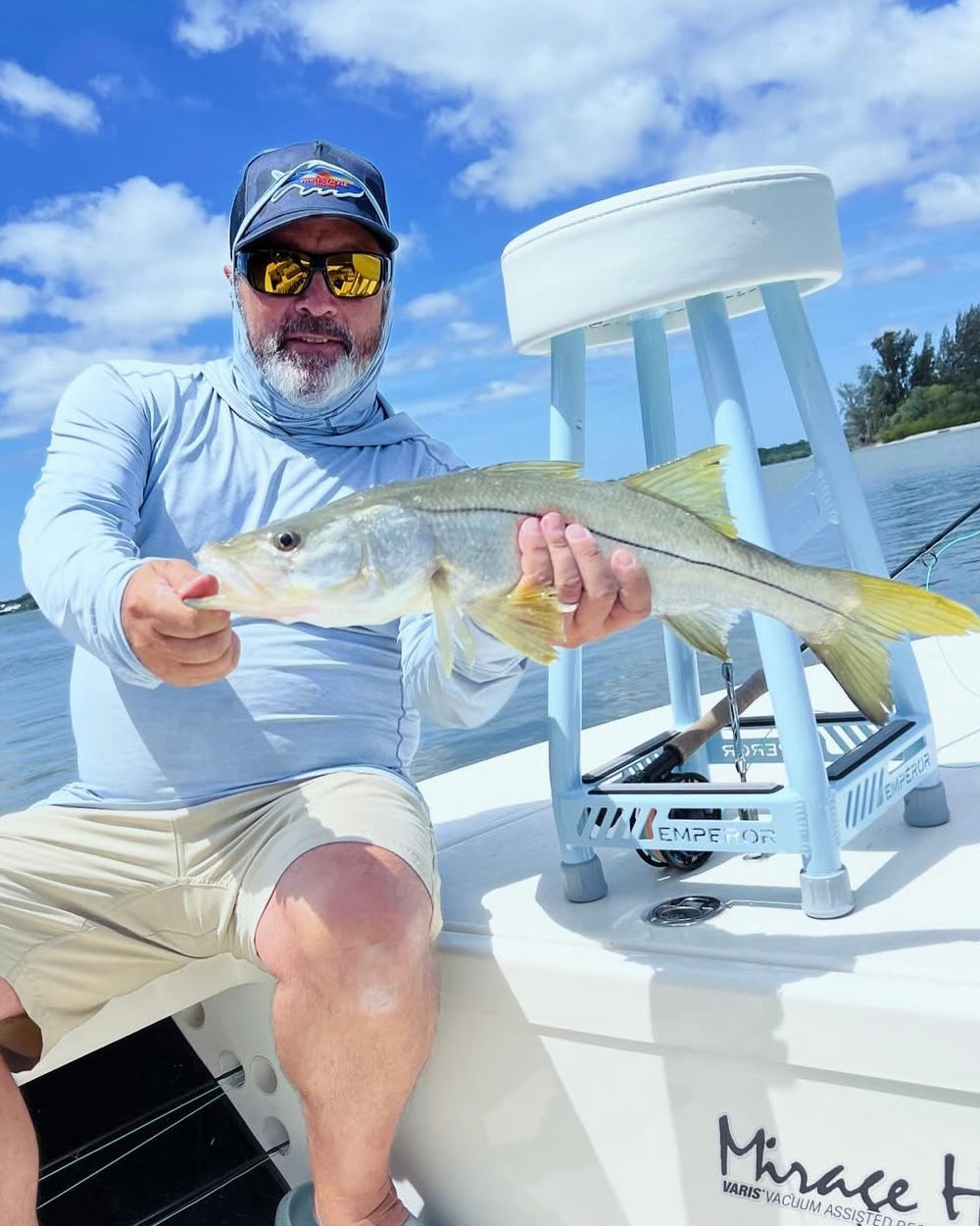 Man holding a snook on a boat with a clear blue sky and water in the background