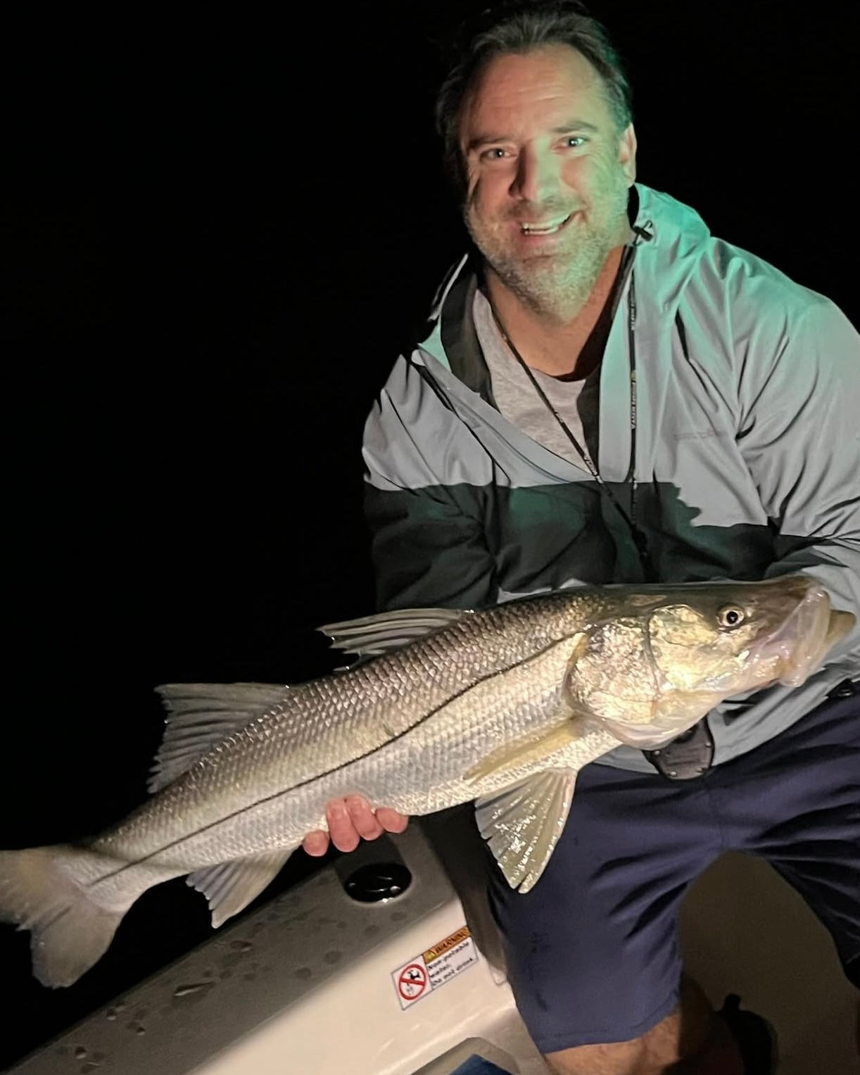 Man holding a large snook at night on a dark background
