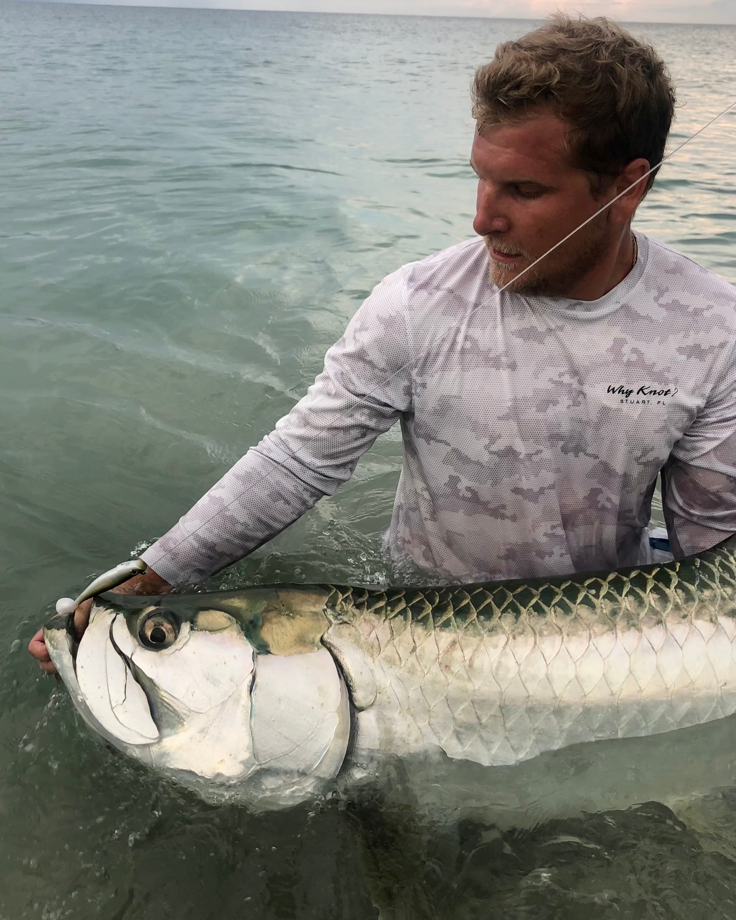 Man holding a large tarpon in the water off the beach 