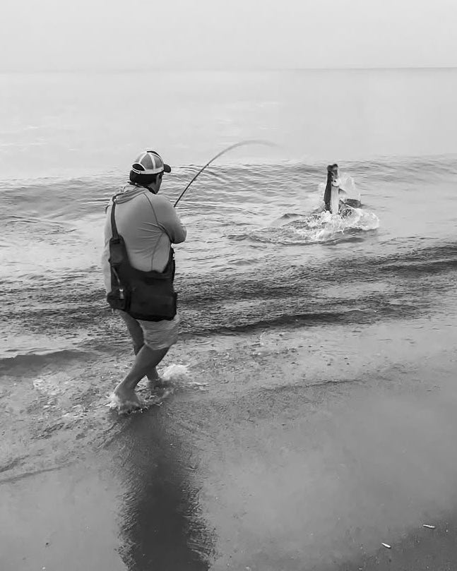 Man on the sand, fighting a tarpon on fly rod at the beach 