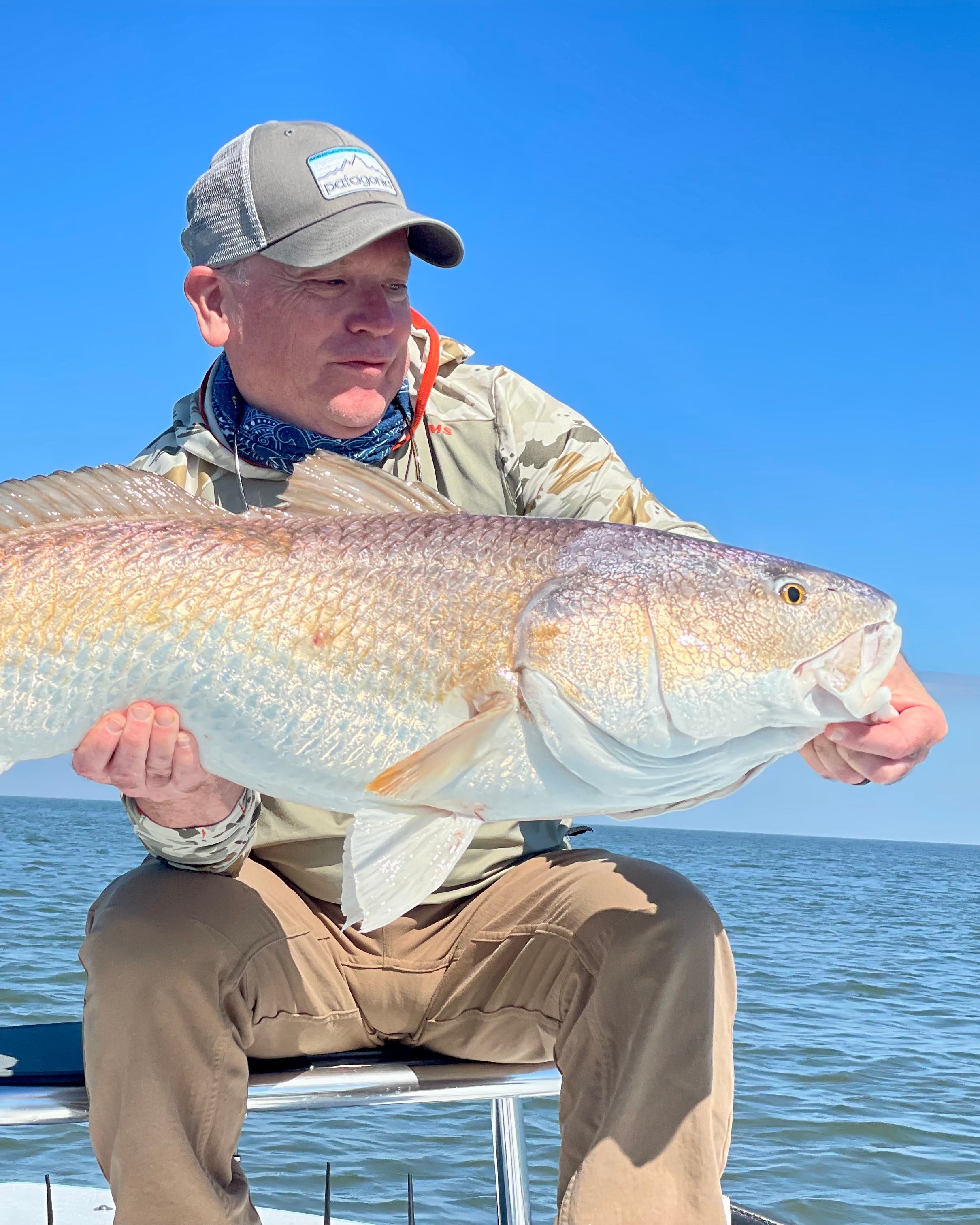 Man holding a large Redfish on a boat with clear blue sky and water in the background