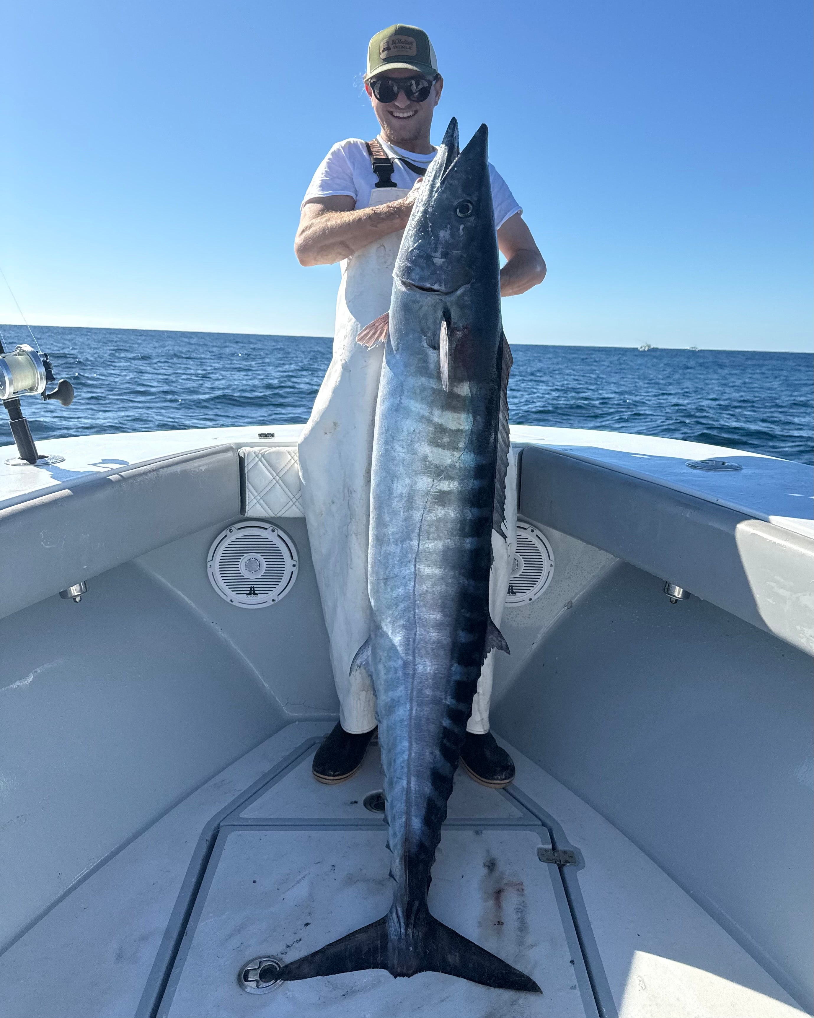 Man holding a large wahoo on a boat with a clear blue sky and ocean background